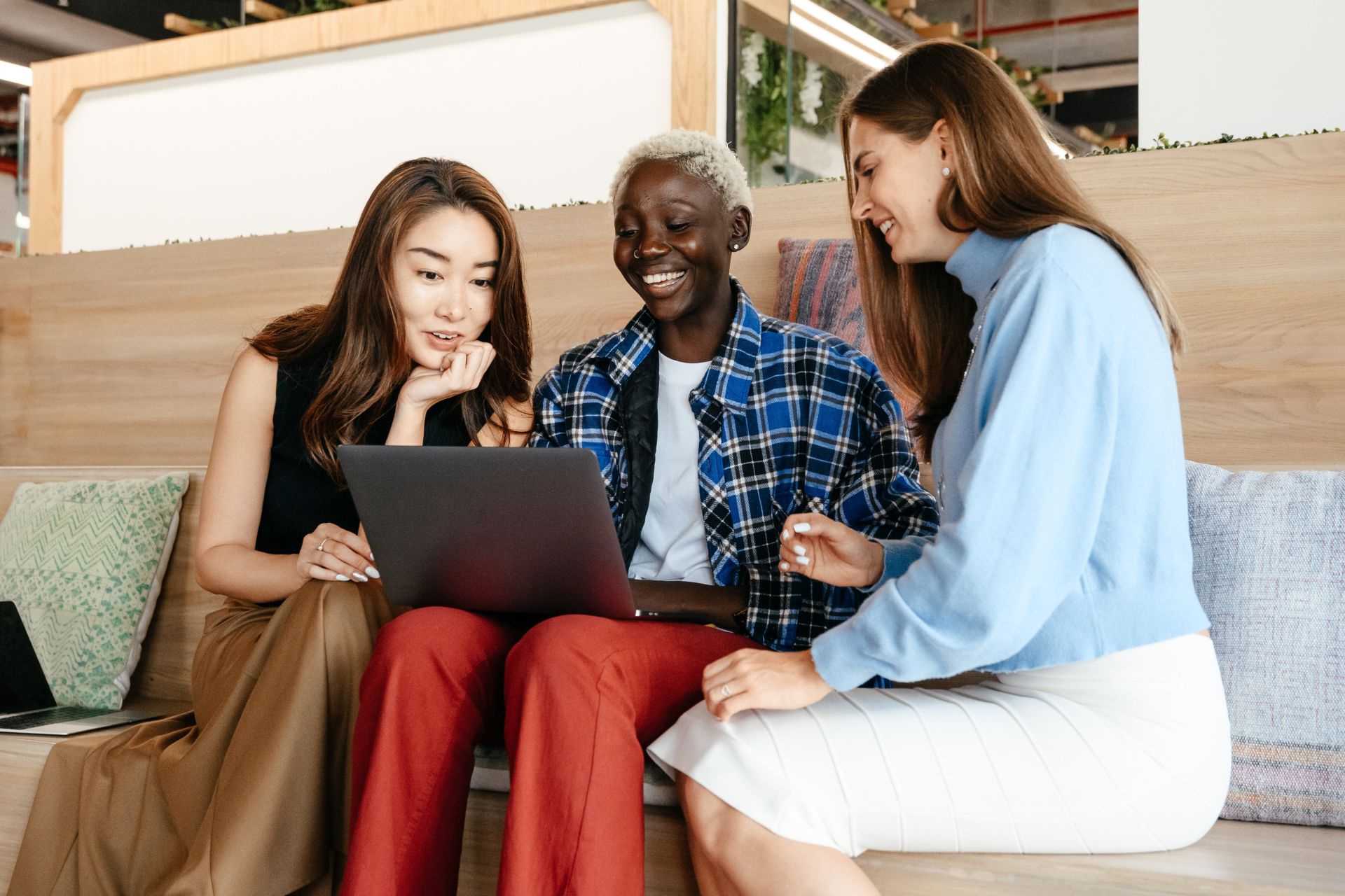 Group of happy trendy multiethnic women surfing internet on netbook while talking and smiling